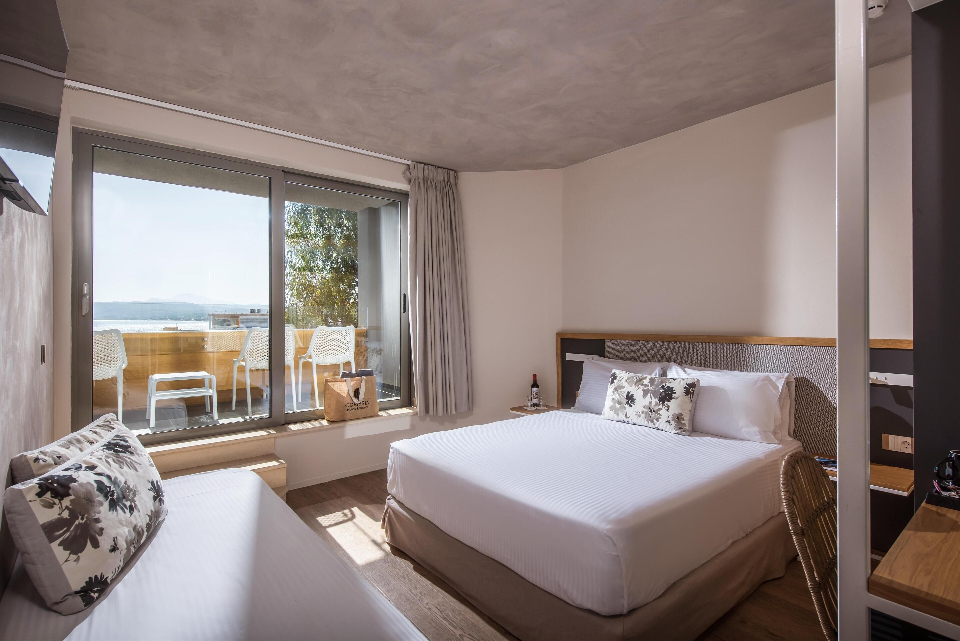 Habitación de hotel con una cama grande, un sofá, zona de comedor con sillas y vistas al exterior.