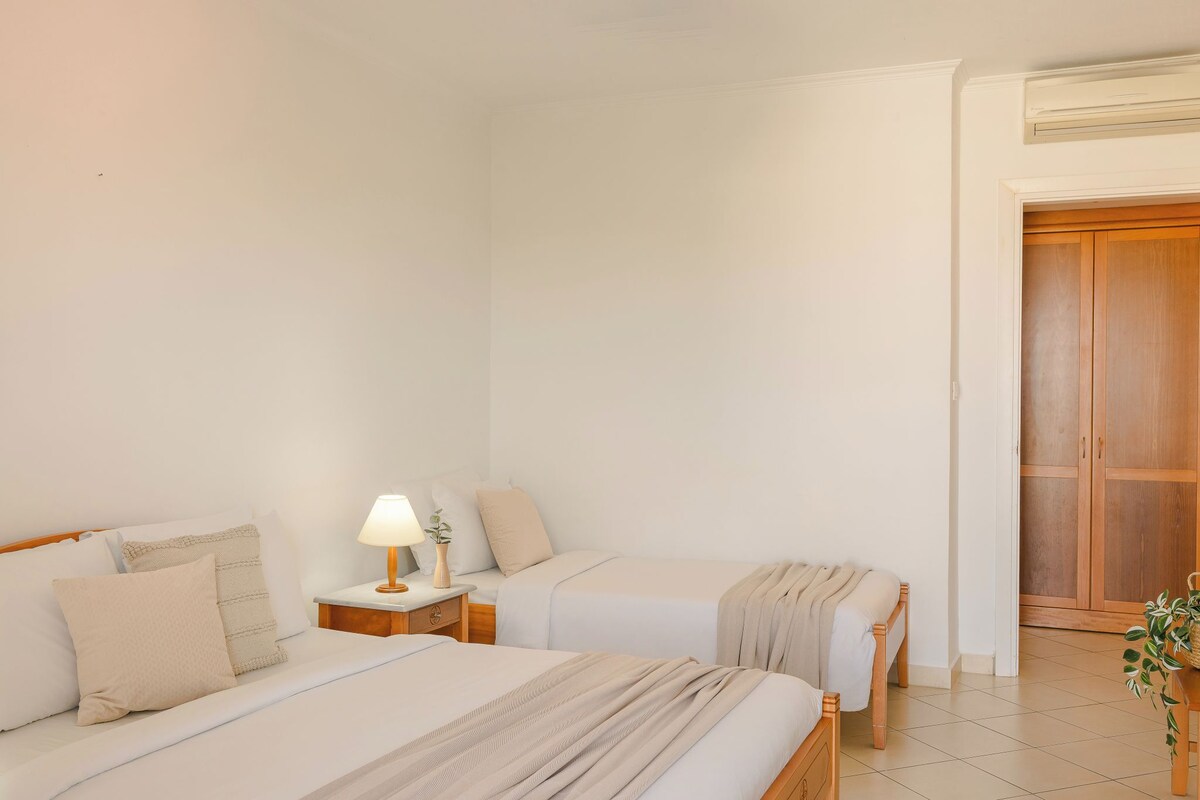 A hotel room with two beds, a bedside table with a lamp, and a wooden wardrobe.