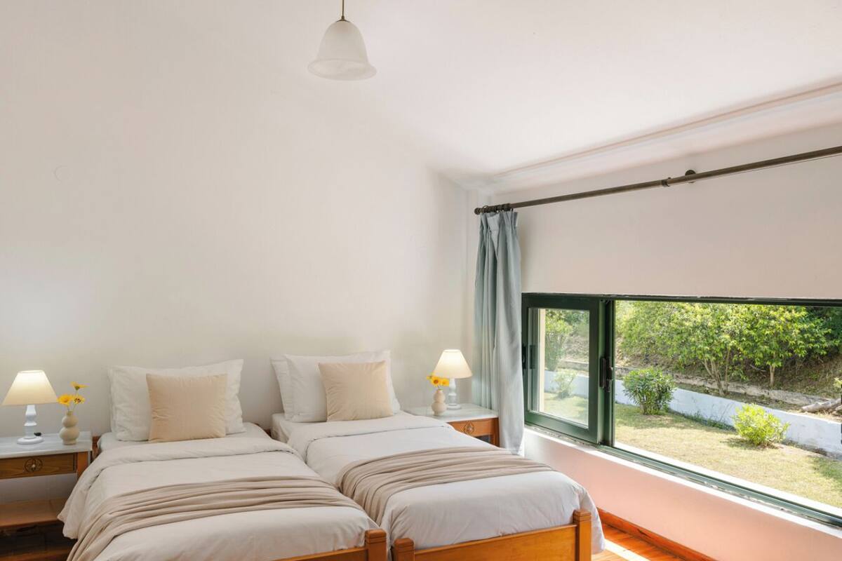 Un dormitorio con dos camas, una ventana con vistas a zonas verdes y una lámpara colgante.