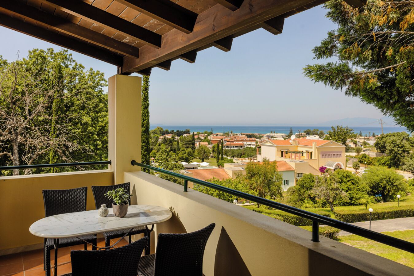 Un balcón con mesa y sillas, con vista a un barrio residencial con casas y árboles.