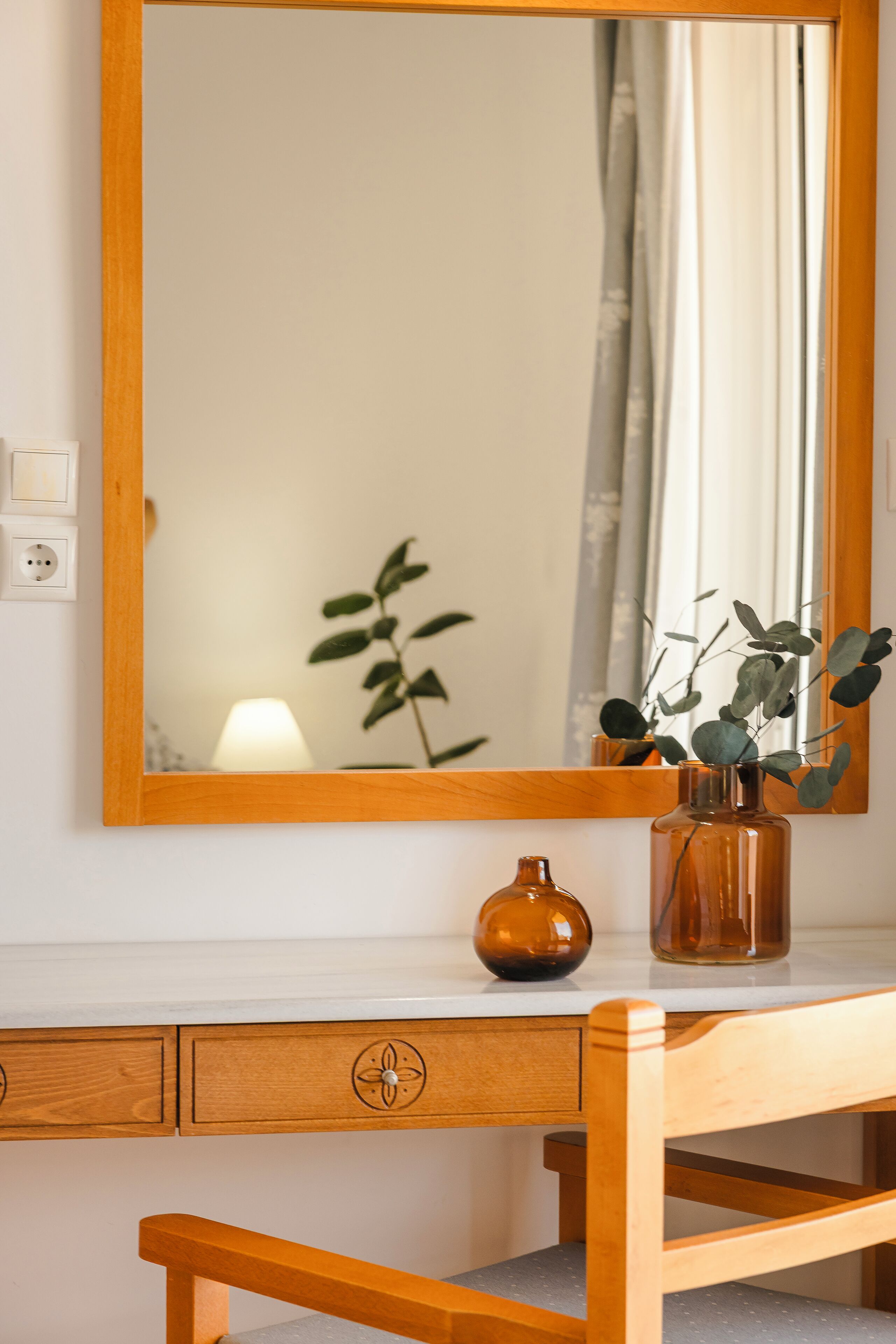 A wooden desk with a mirror, a vase with a plant, and a lamp.