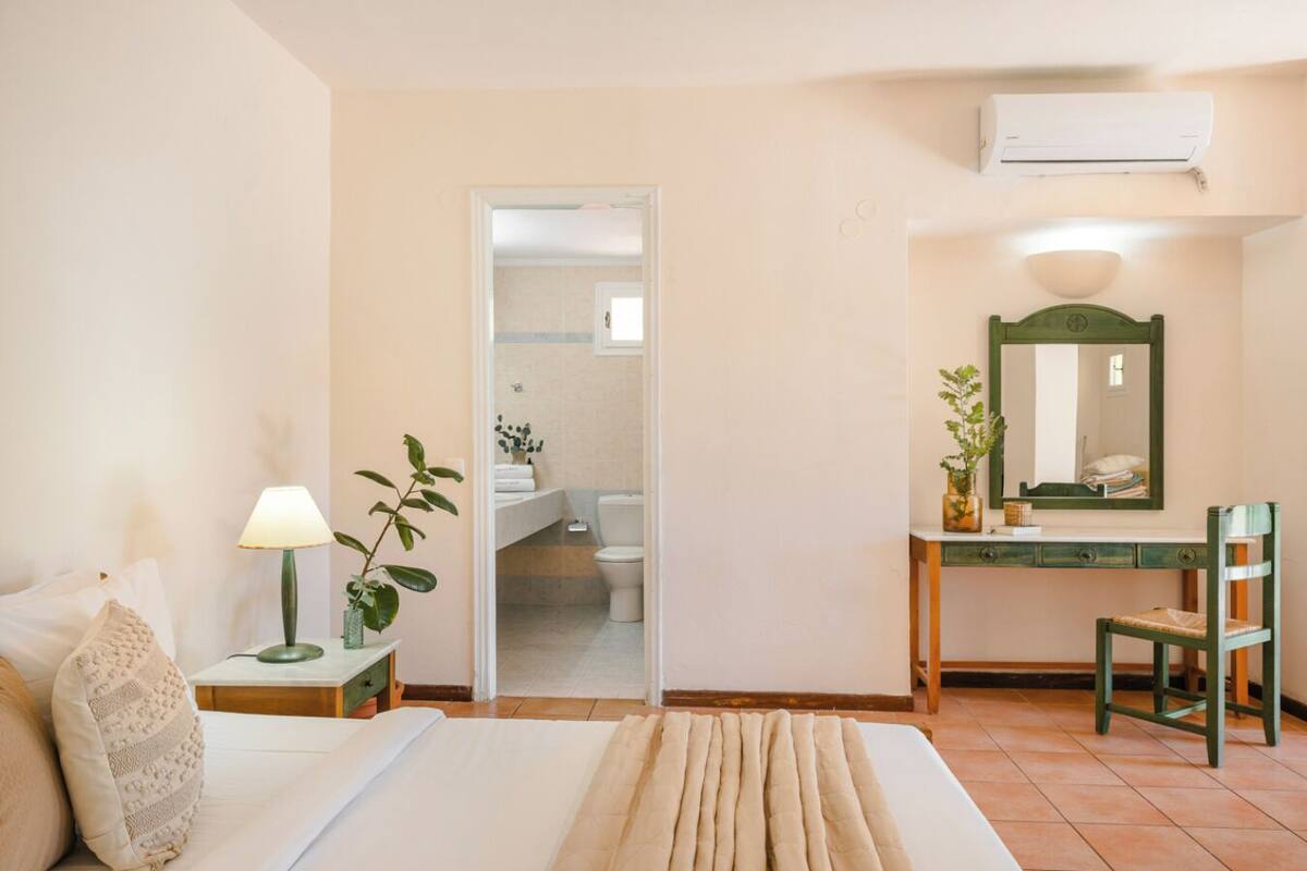 Un dormitorio con cama, lámpara de noche, cómoda, espejo y unidad de aire acondicionado.