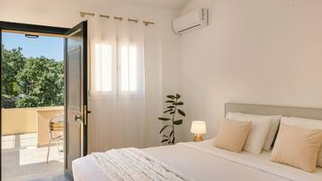A hotel room with a bed, a bedside lamp, a potted plant, and a view of the outdoors.