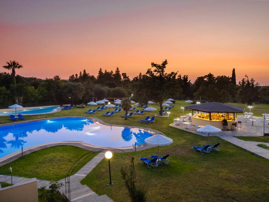Un área de piscina con sillones y sombrillas, rodeada de árboles y un pabellón.