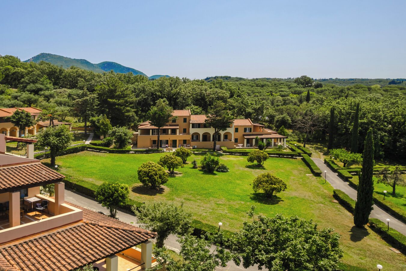A large, multi-story building with a courtyard, surrounded by lush greenery and hills in the background.
