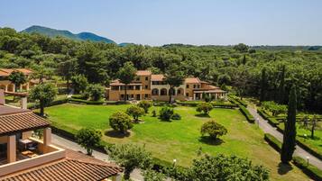 A large, multi-story building with a courtyard, surrounded by lush greenery and hills in the background.