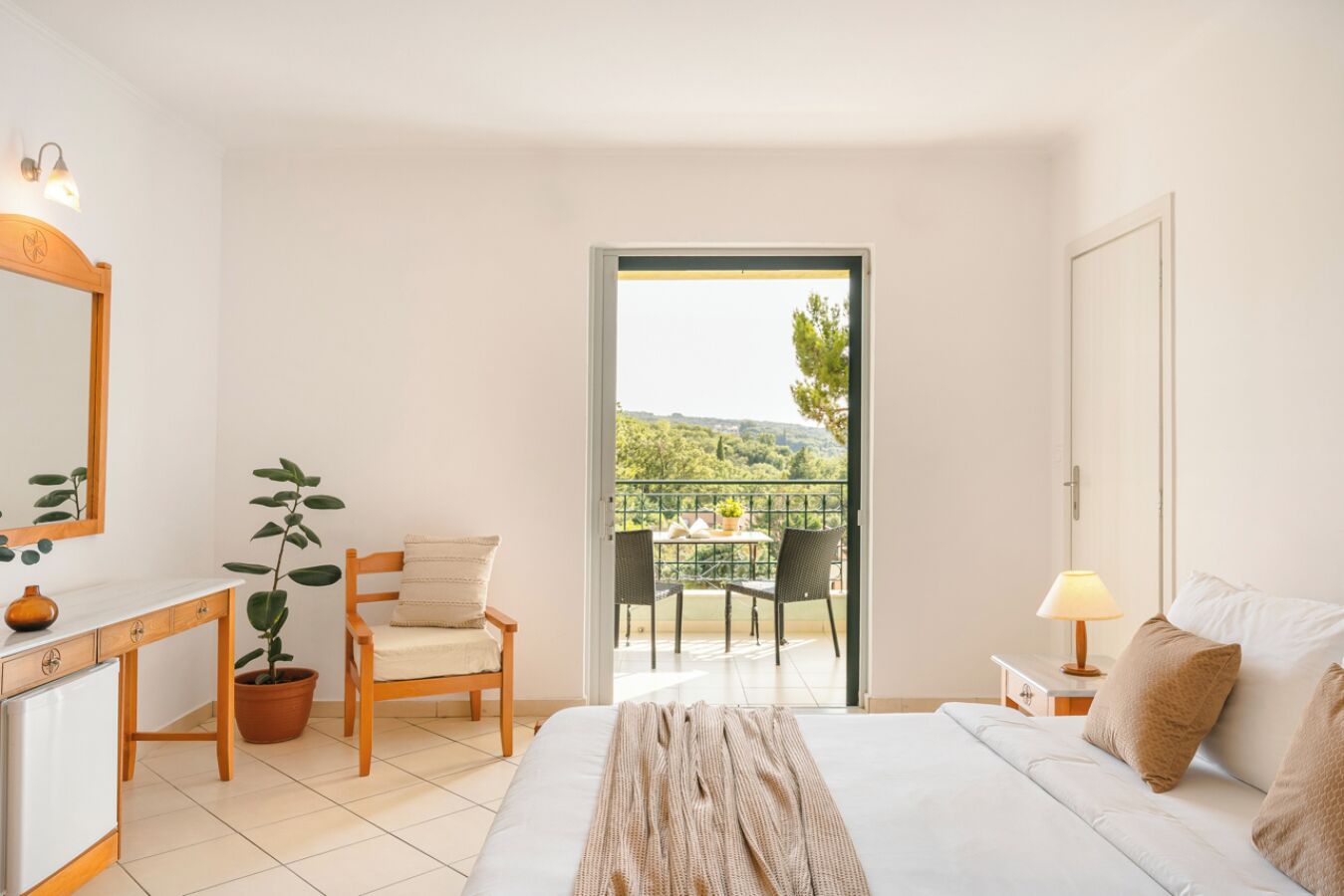 Un dormitorio con cama, escritorio, silla, planta en maceta y balcón con vistas a follaje.