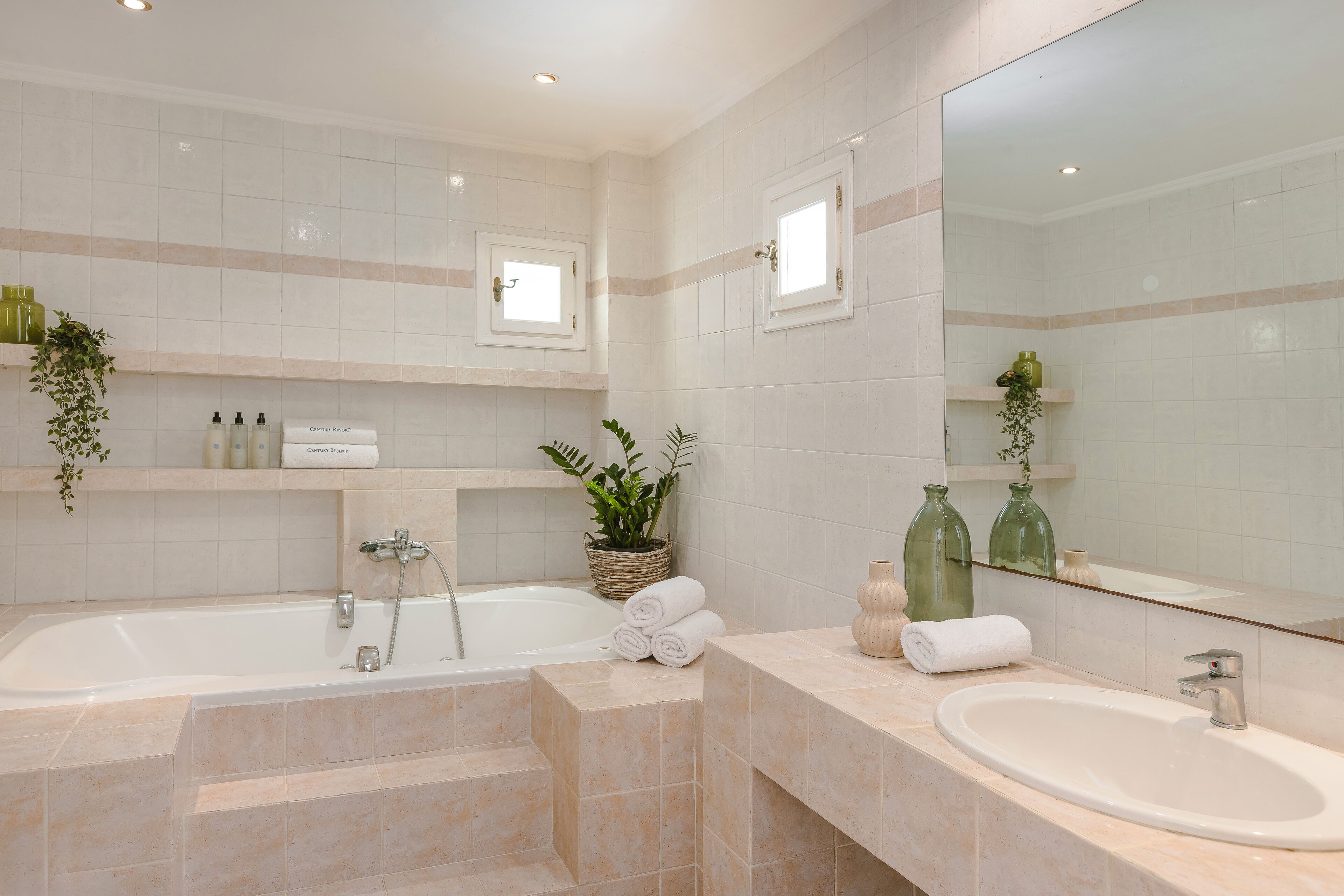 Un bagno moderno con una vasca, un lavabo e uno specchio grande. Ci sono piante e articoli da toilette sugli scaffali.