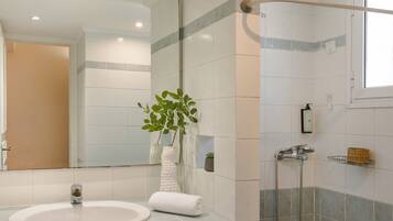 A bathroom with a sink, mirror, shower, and a plant.