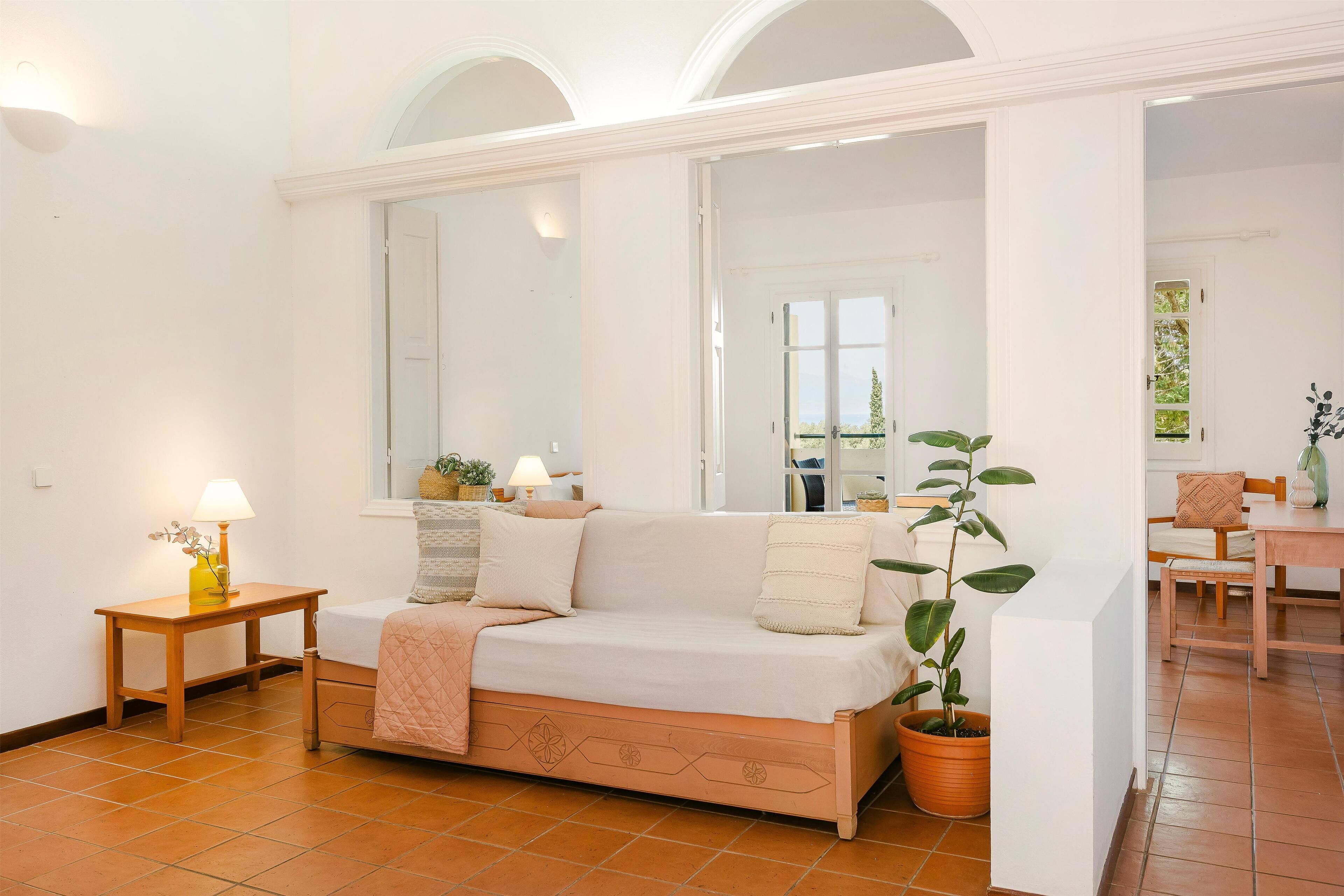 A cozy room with a wooden sofa, a small table with a lamp, and a potted plant.