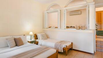 A room with two beds, a small table, a lamp, and a window with a view of the outside.