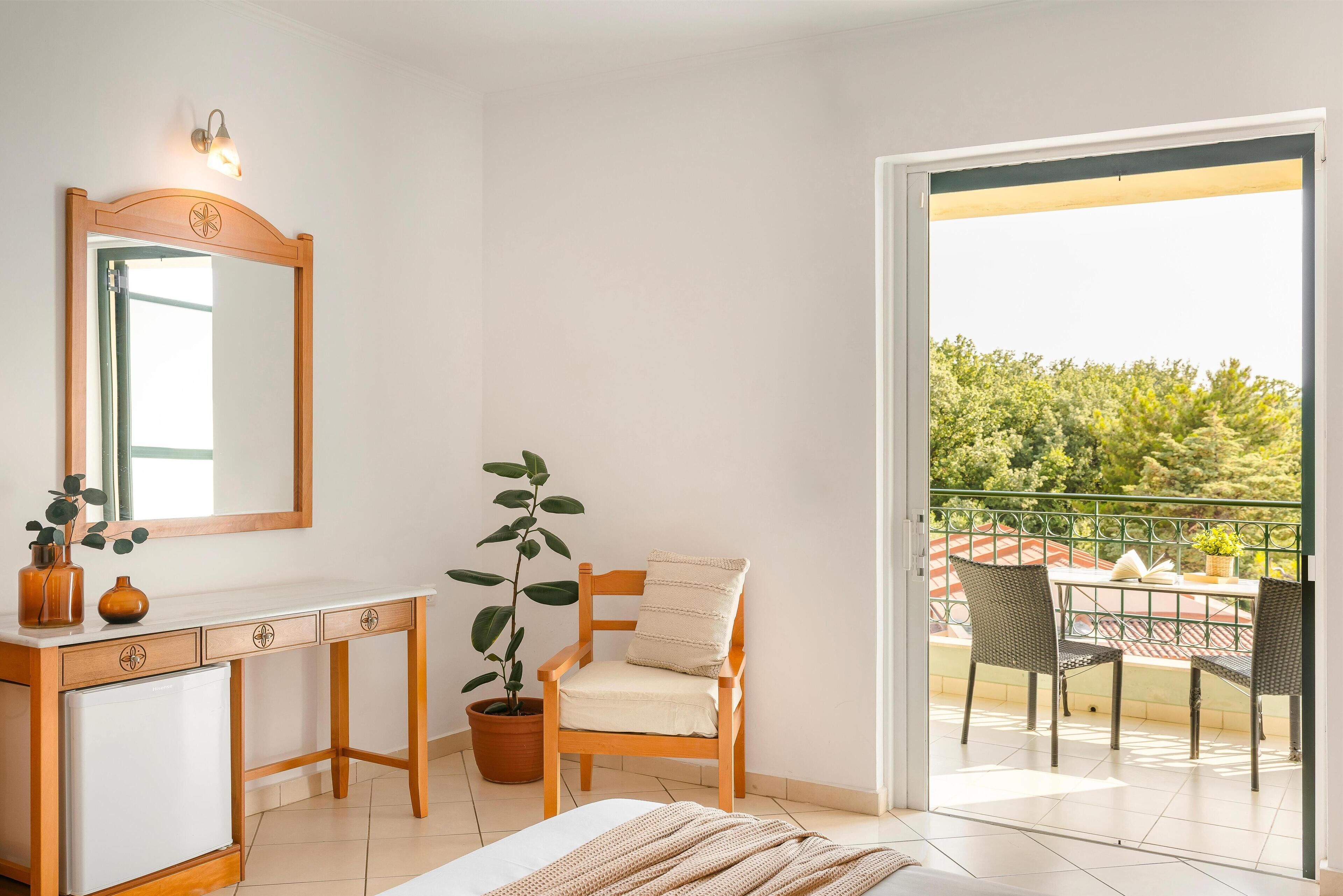 A bedroom with a bed, a wooden desk, a chair, a potted plant, and a balcony with outdoor furniture.