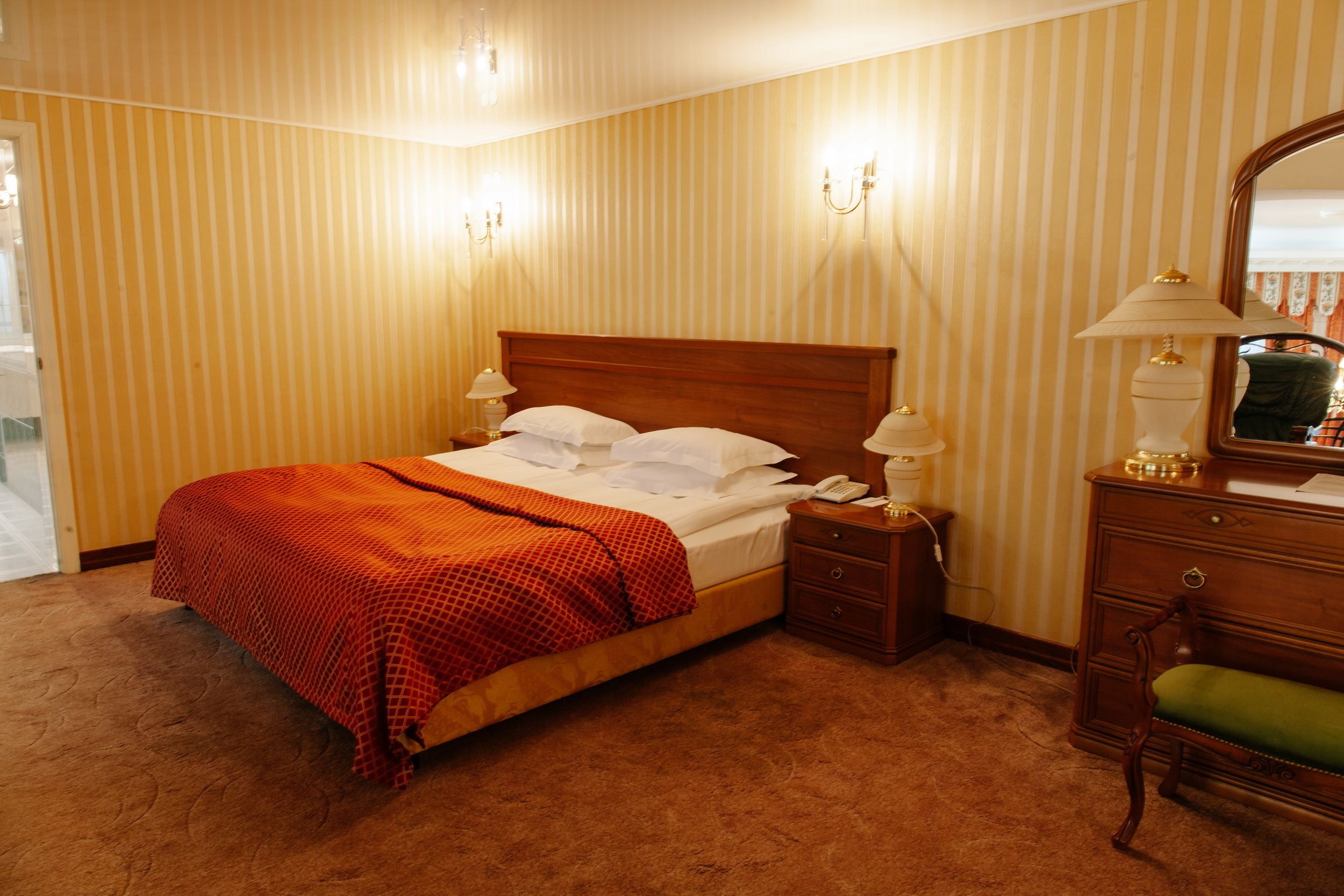 A hotel room with a wooden bed, two bedside lamps, a nightstand, a green chair, and a mirror.