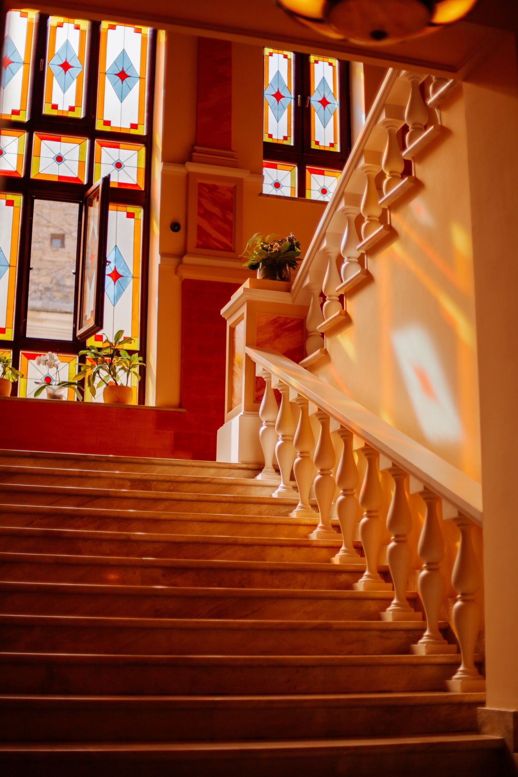 Un escalier orné de balustres et doté d’une main courante, menant à un palier où se trouve un pot de fleurs.