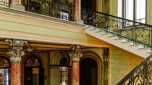 A grand staircase with ornate black railings, marble columns, and a patterned carpet. - Londonskaya Hotel (Odesa)
