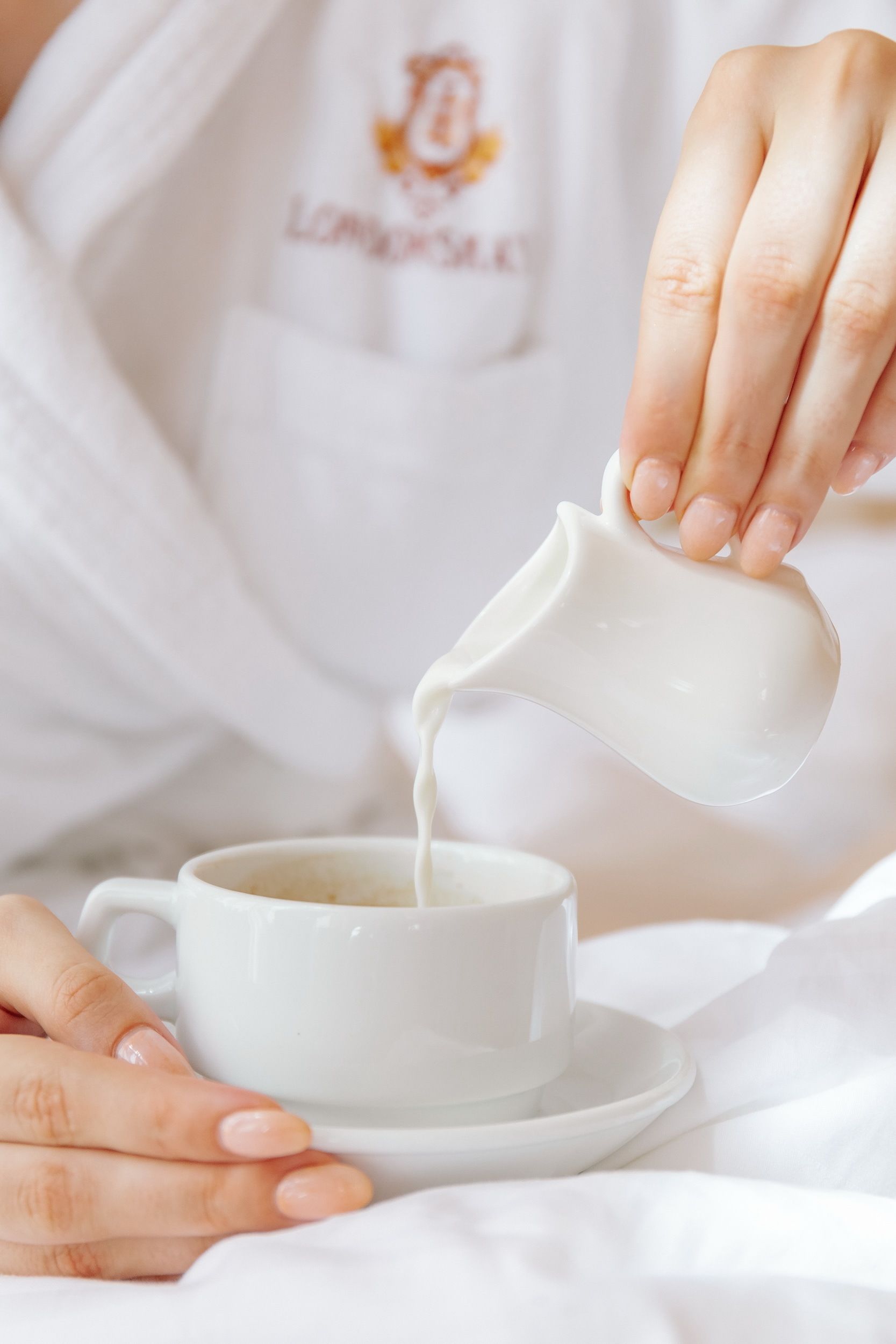 A person pouring milk into a white cup on a saucer.