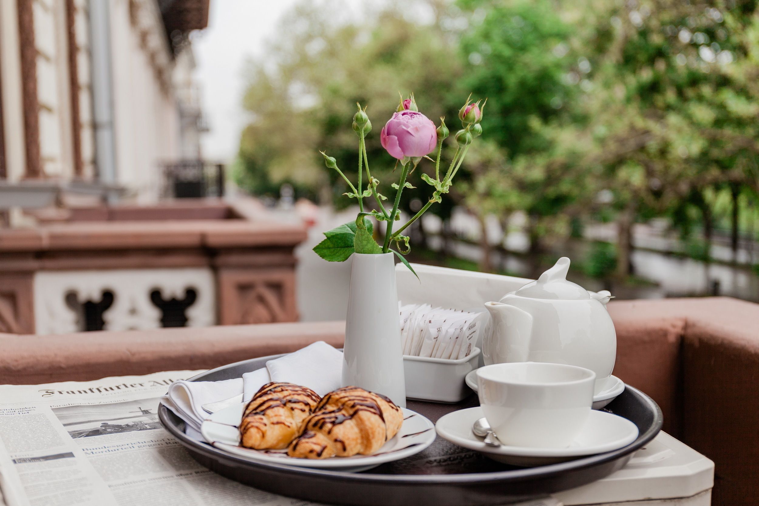 A tray with croissants, a teapot, and a cup on a table with newspapers.