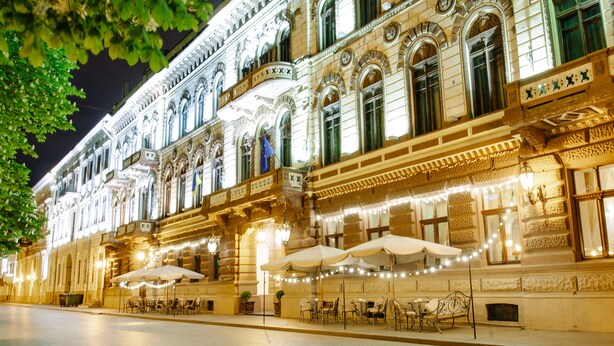 A historic building with ornate architecture, outdoor seating with umbrellas, and string lights. - Londonskaya Hotel (Odesa)