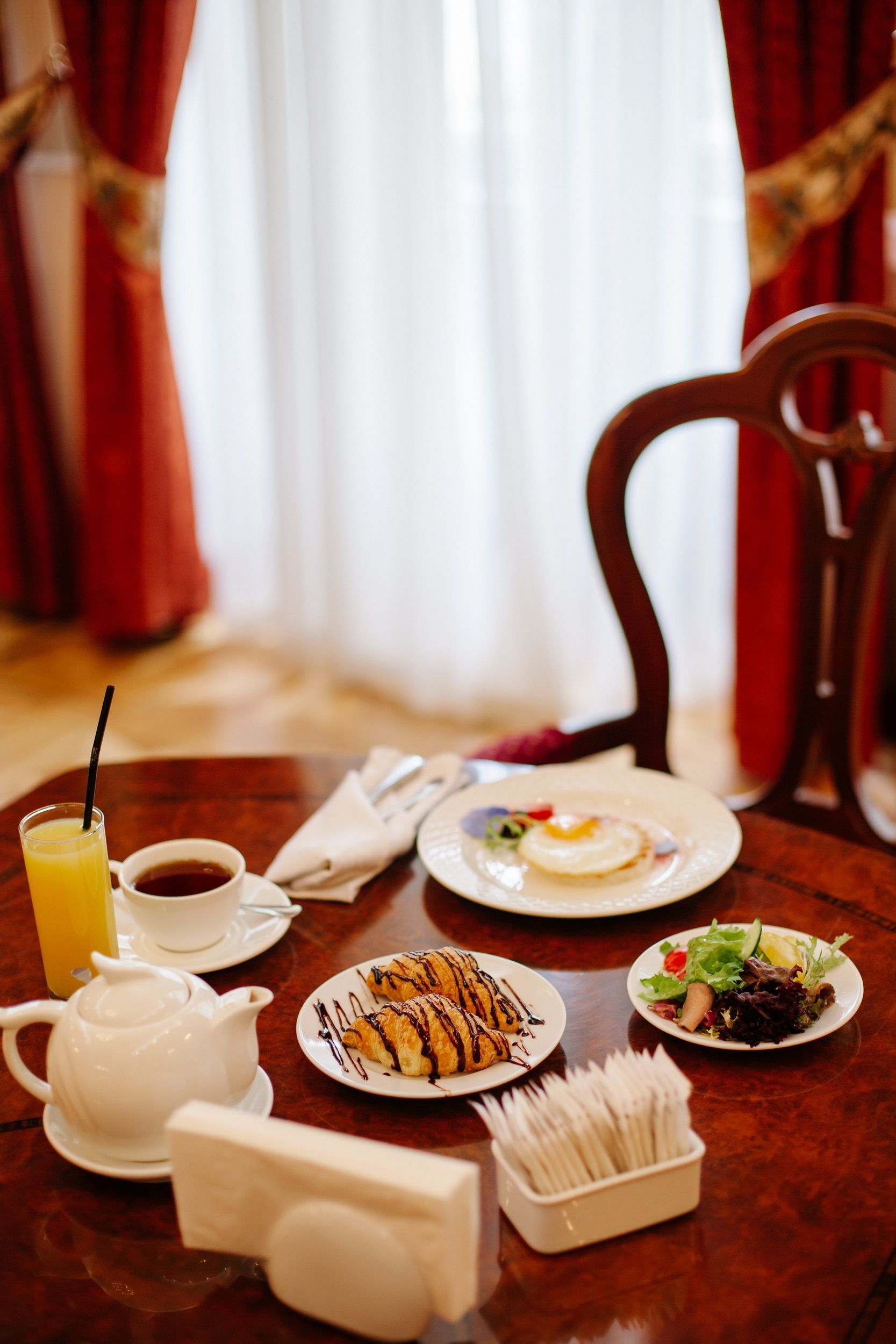 Ein Esstisch mit Frühstücksangeboten, darunter ein Teekessel, Tassen, eine Platte Croissants, eine Eierspeise und ein Salat.