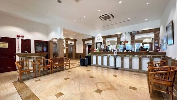 A lobby with a reception desk, wooden chairs, and a tiled floor.