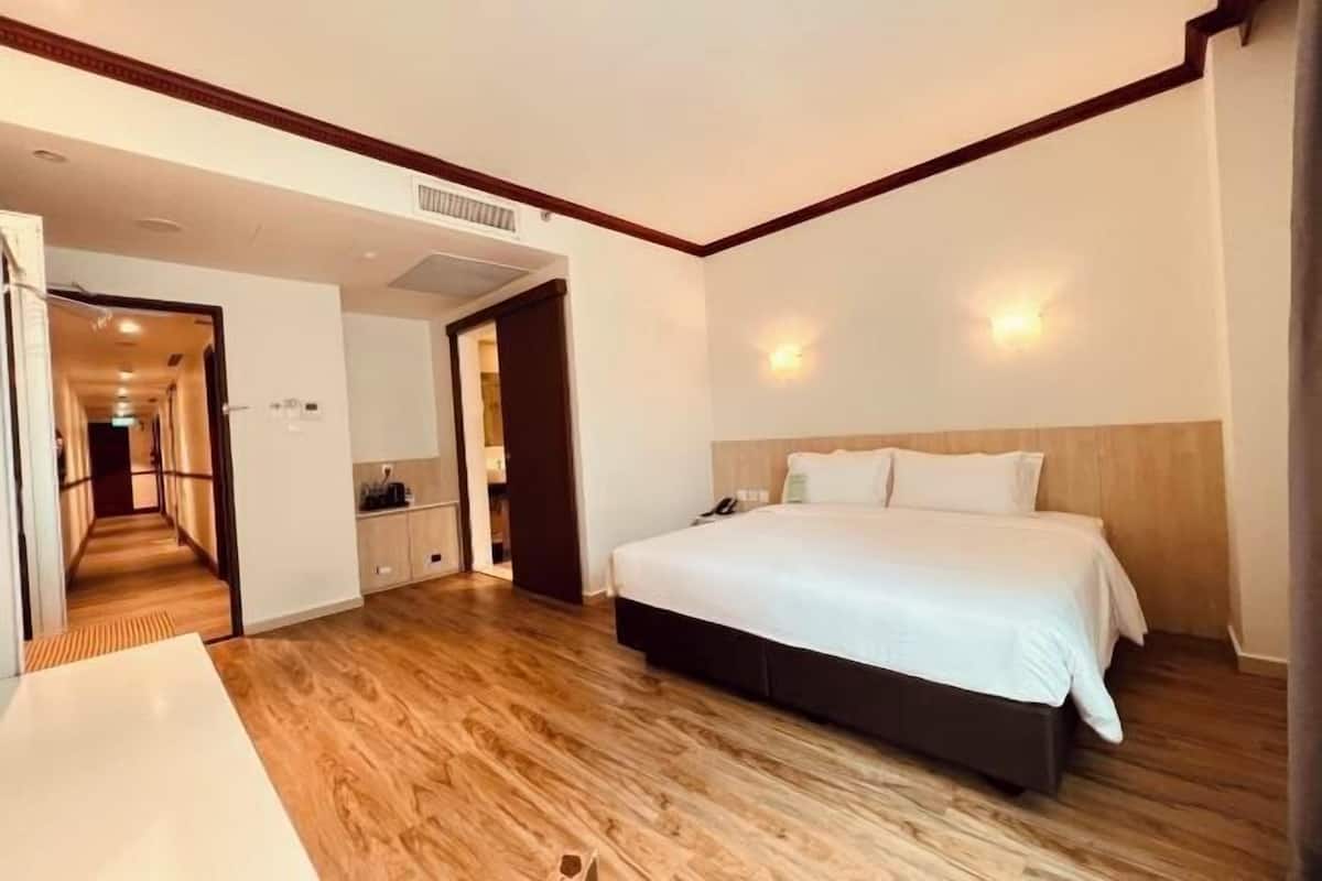 Een hotelkamer met een houten vloer, een groot bed met wit beddengoed, een nachtkastje en een kledingkast.