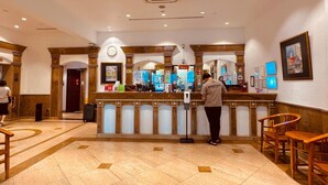 Eine Hotelhalle mit einer Rezeption, einer Uhr und einem digitalen Bildschirm.