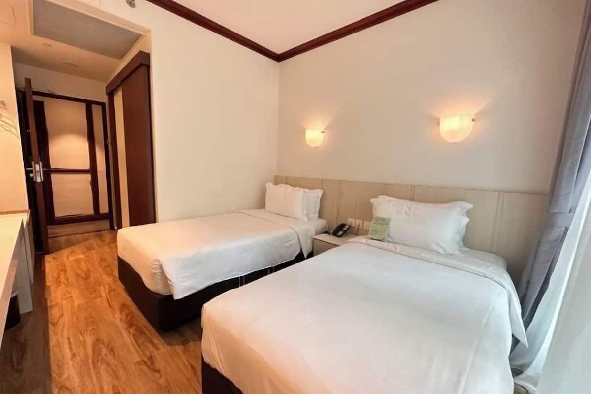 Een hotelkamer met twee bedden, een houten vloer, een houten hoofdbord en een nachtkastje met telefoon en lamp.