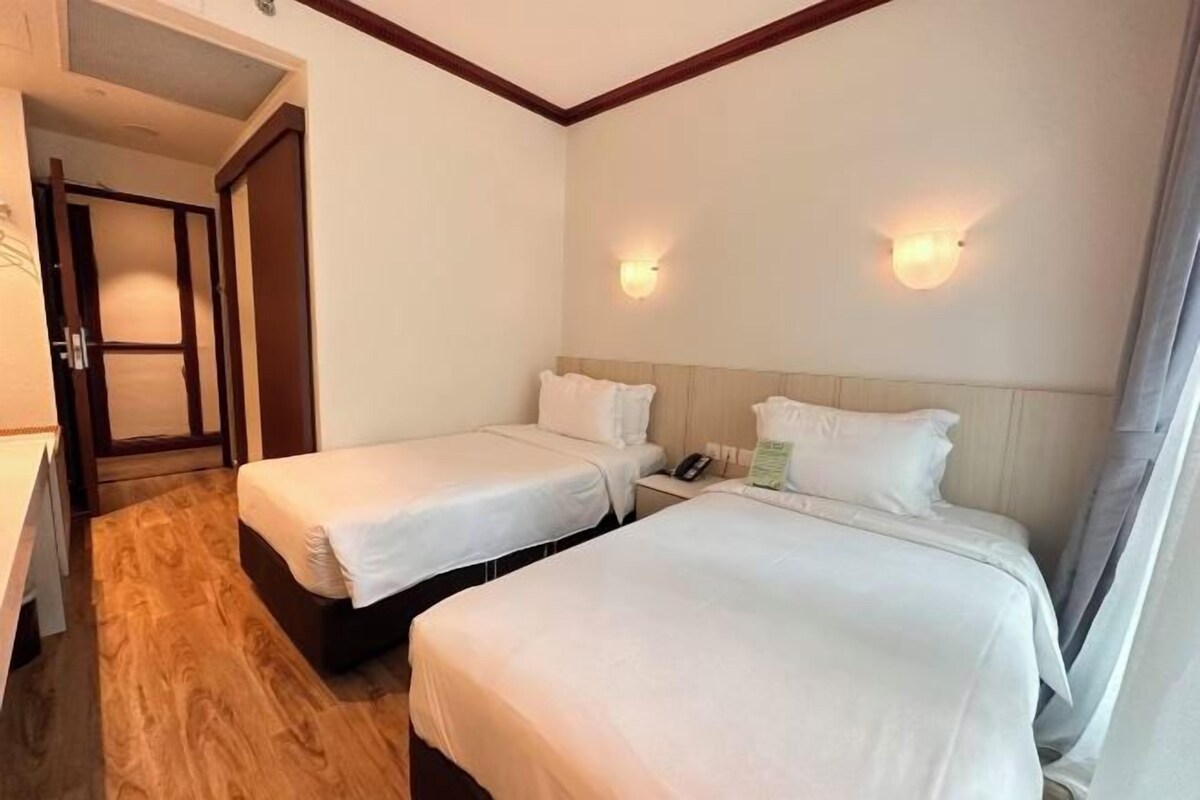 A hotel room with two beds, a wooden floor, a wooden headboard, and a nightstand with a phone and a lamp.