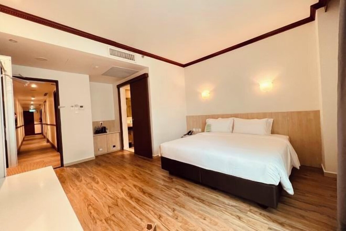 A hotel room with a wooden floor, a large bed with white bedding, a bedside table, and a wardrobe.