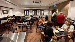A restaurant with multiple tables and chairs, people dining, and a counter area.