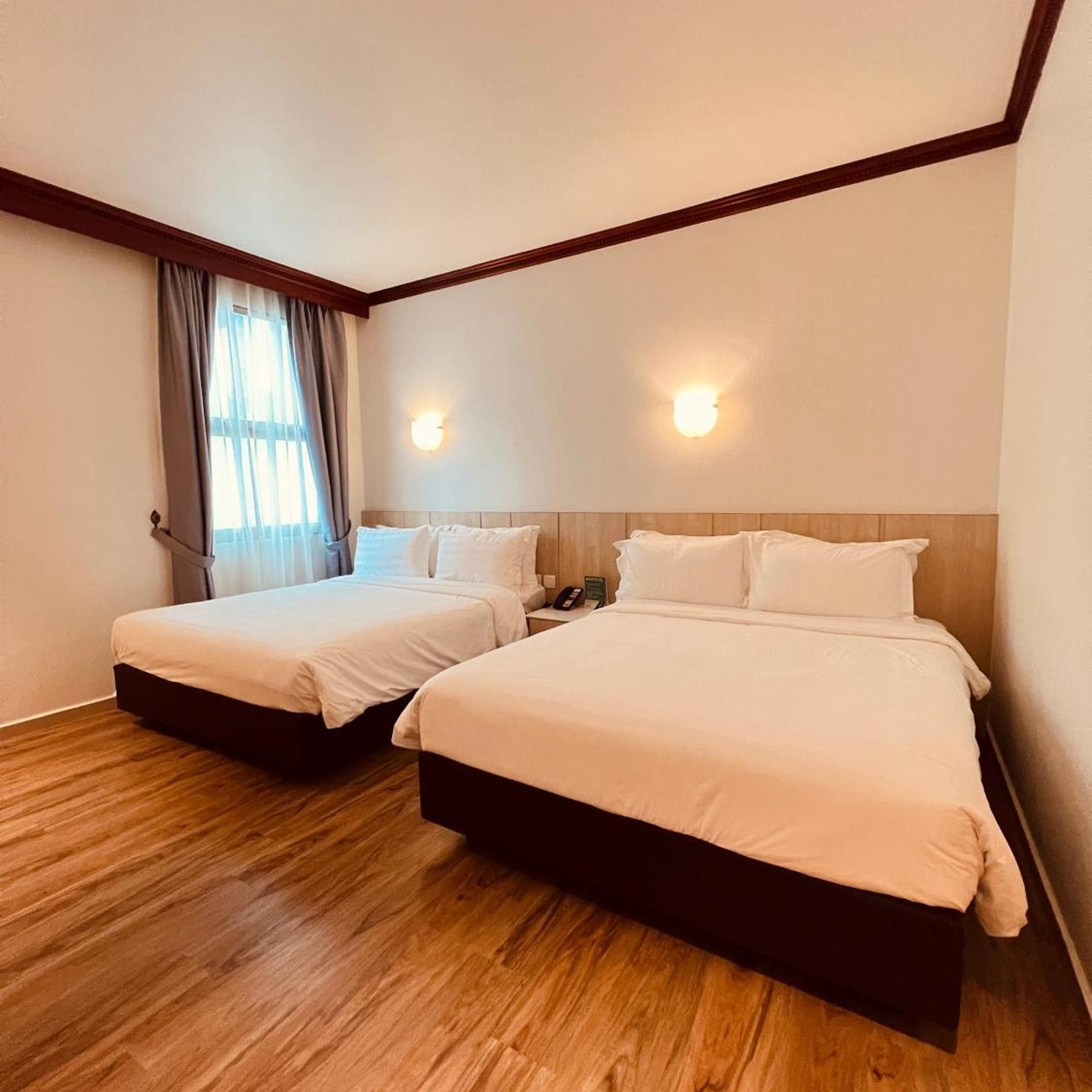 Habitación de hotel con dos camas, suelo de madera y una ventana con cortinas.
