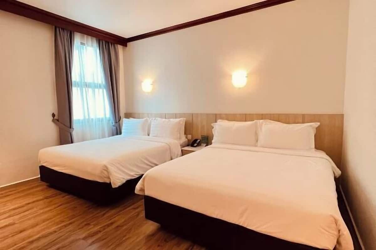 Een hotelkamer met twee bedden, houten vloeren, een raam met gordijnen en wandlampen.