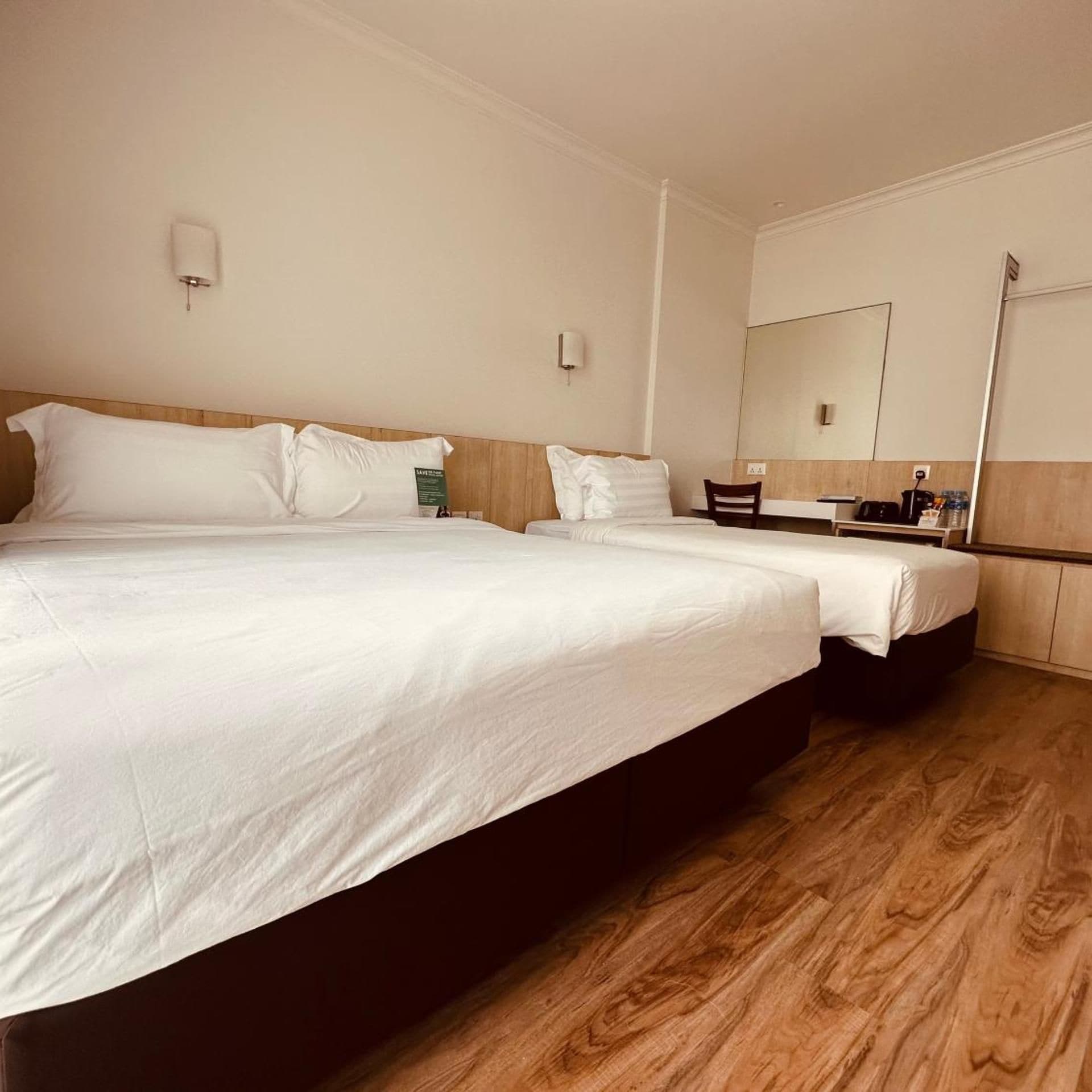 A hotel room with a large bed, a bedside table, a mirror, and a wooden floor.