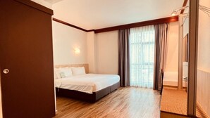 Ein Hotelzimmer mit Bett, Holzboden, Fenster mit Vorhängen und einer Tür.