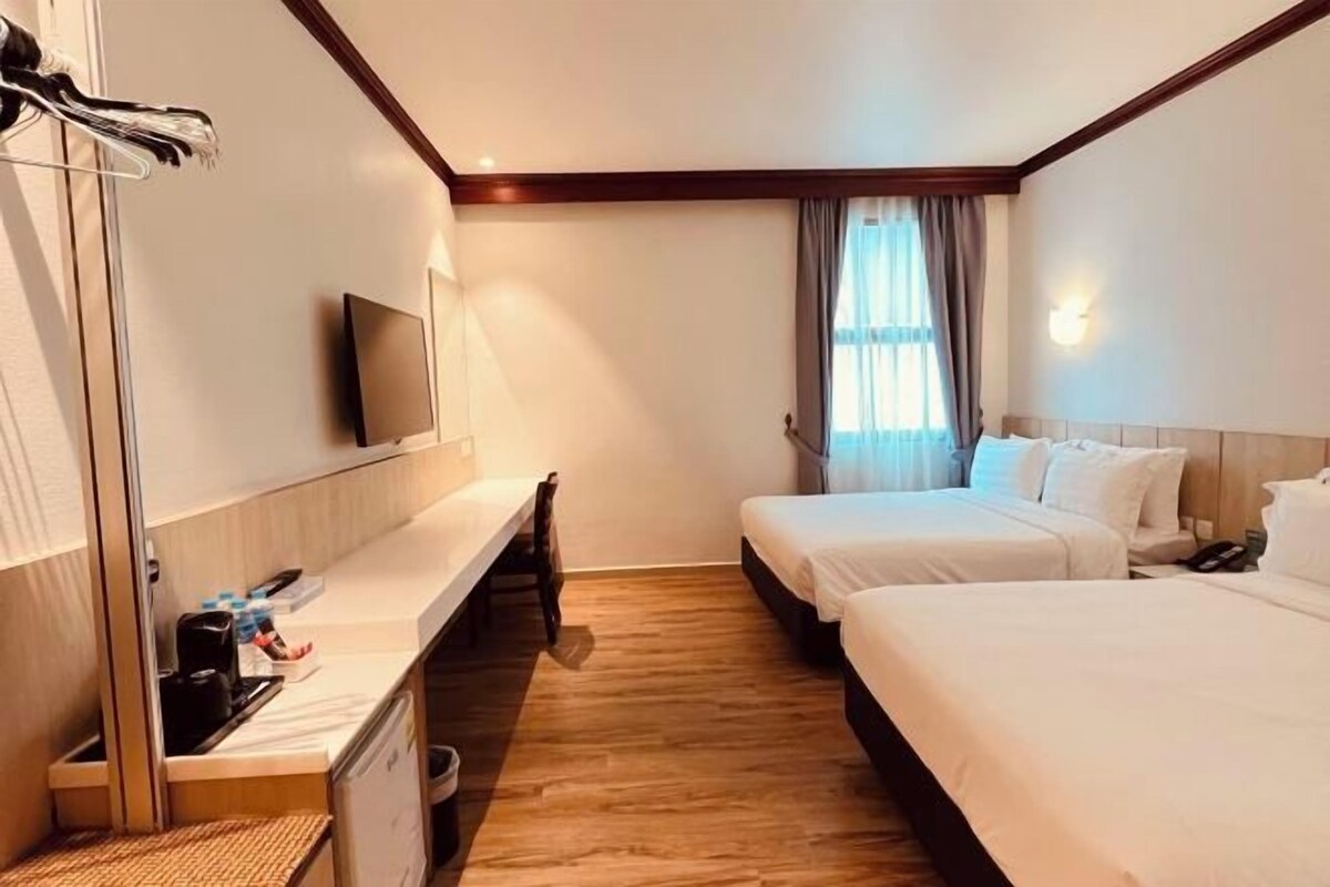 A hotel room with two beds, a TV, a desk with a chair, and a window with curtains.