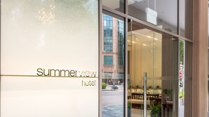 A modern hotel entrance with a glass facade, a visible reception area, and a stone and plant display. - Summer View Hotel (Singapore)