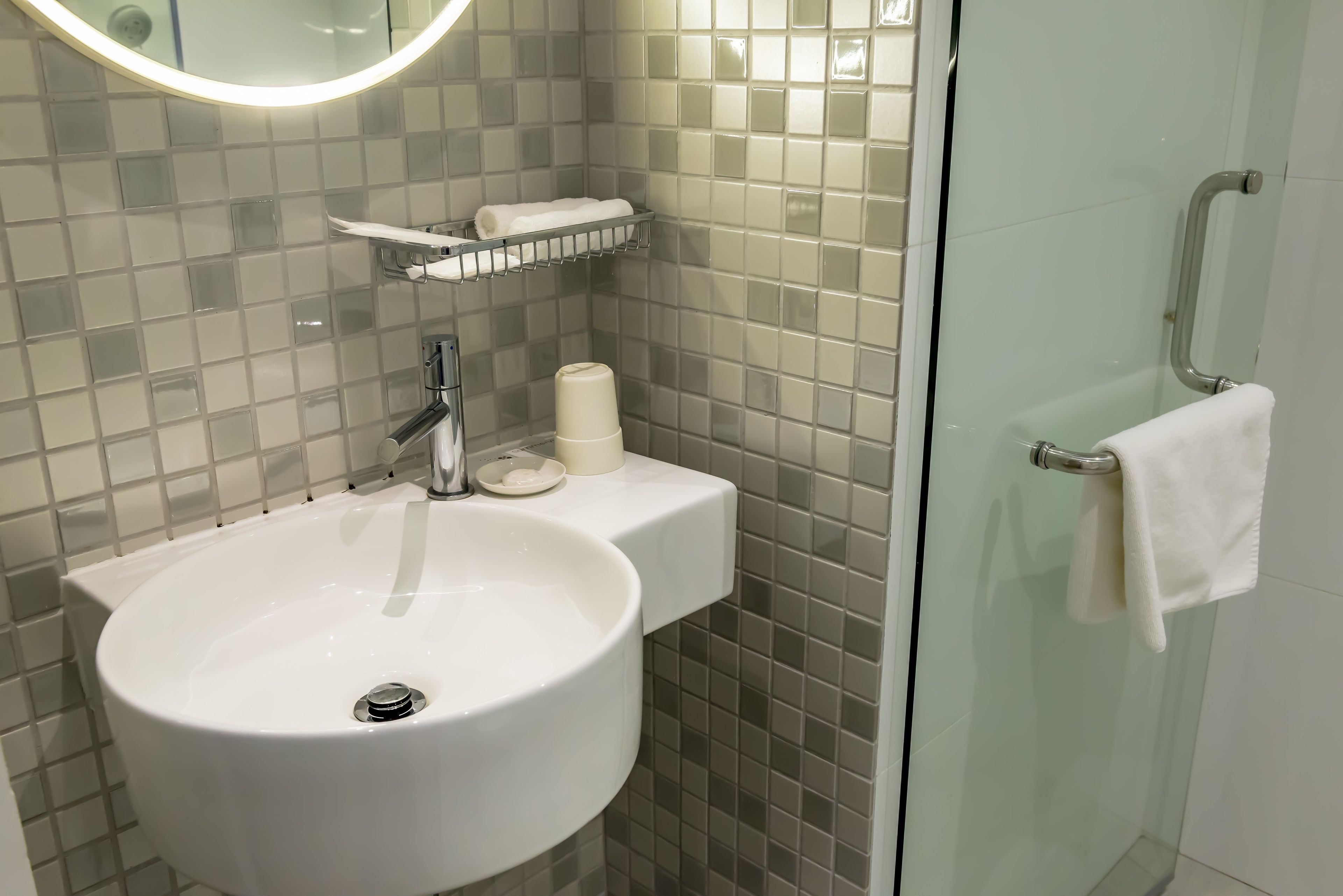 A bathroom with a white sink, a mirror, a towel rack, and a glass shower enclosure.