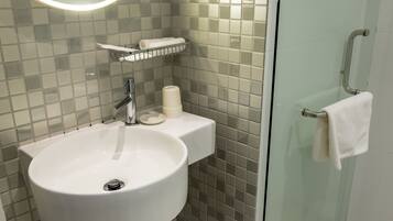A bathroom with a white sink, a mirror, a towel rack, and a glass shower enclosure.