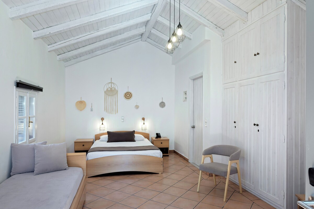 Un dormitorio espacioso con una cama grande, una silla, un armario y un techo con vigas a la vista.