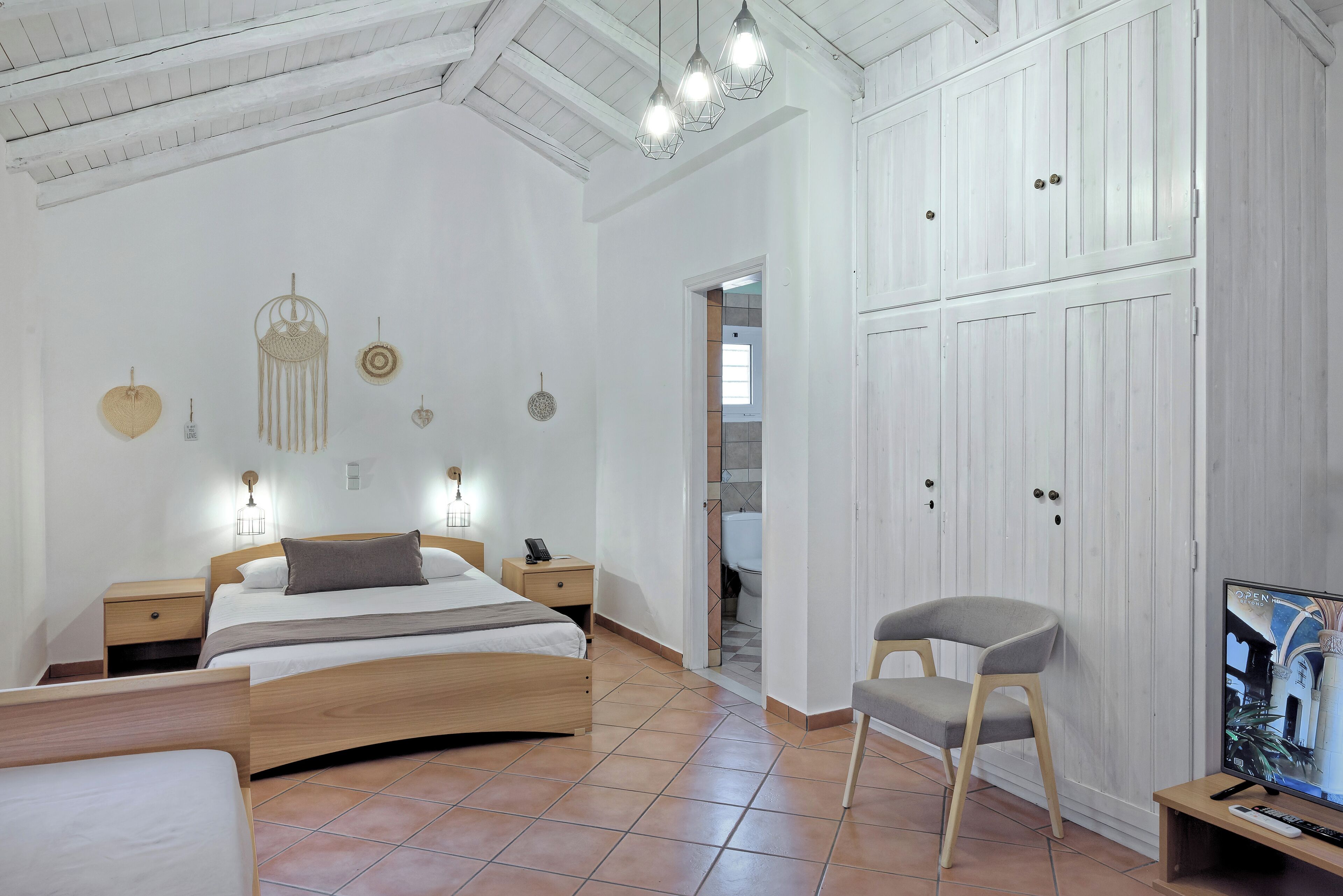 A bedroom with a wooden bed, bedside tables, a chair, a TV, and a wardrobe.