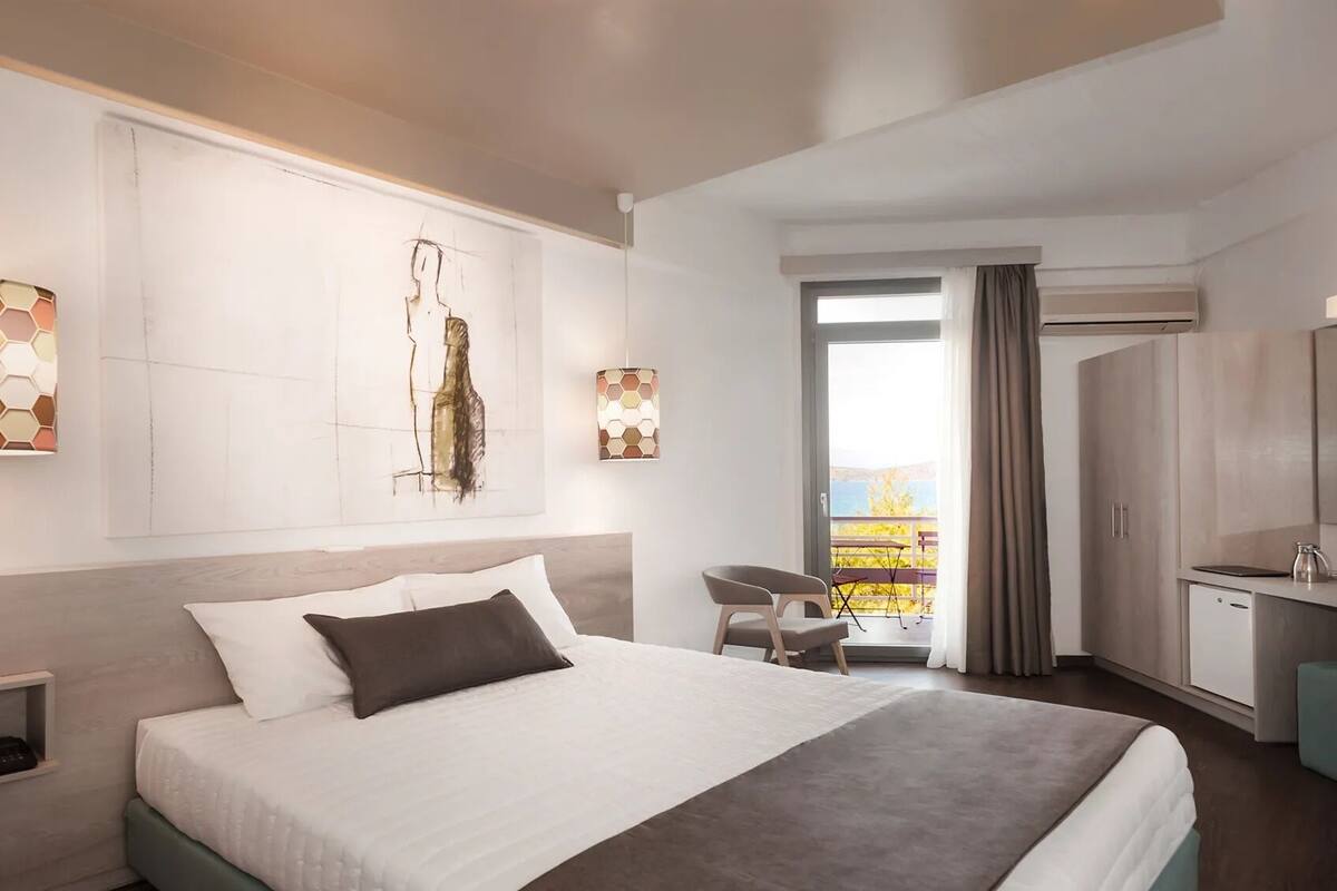 A modern hotel room with a large bed, a desk, and a view of the outdoors.