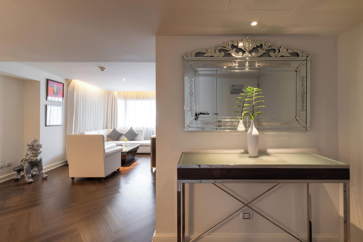 A modern living room with a white sofa, a glass coffee table, and a decorative mirror above it.