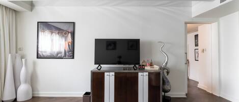 A modern living room with a wooden herringbone floor, a dark wooden cabinet with white handles, a flat-screen TV, and a decorative swan sculpture.