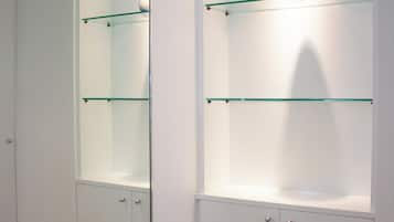 A room with a mirrored wall, a white cabinet with glass shelves, and a wooden floor.