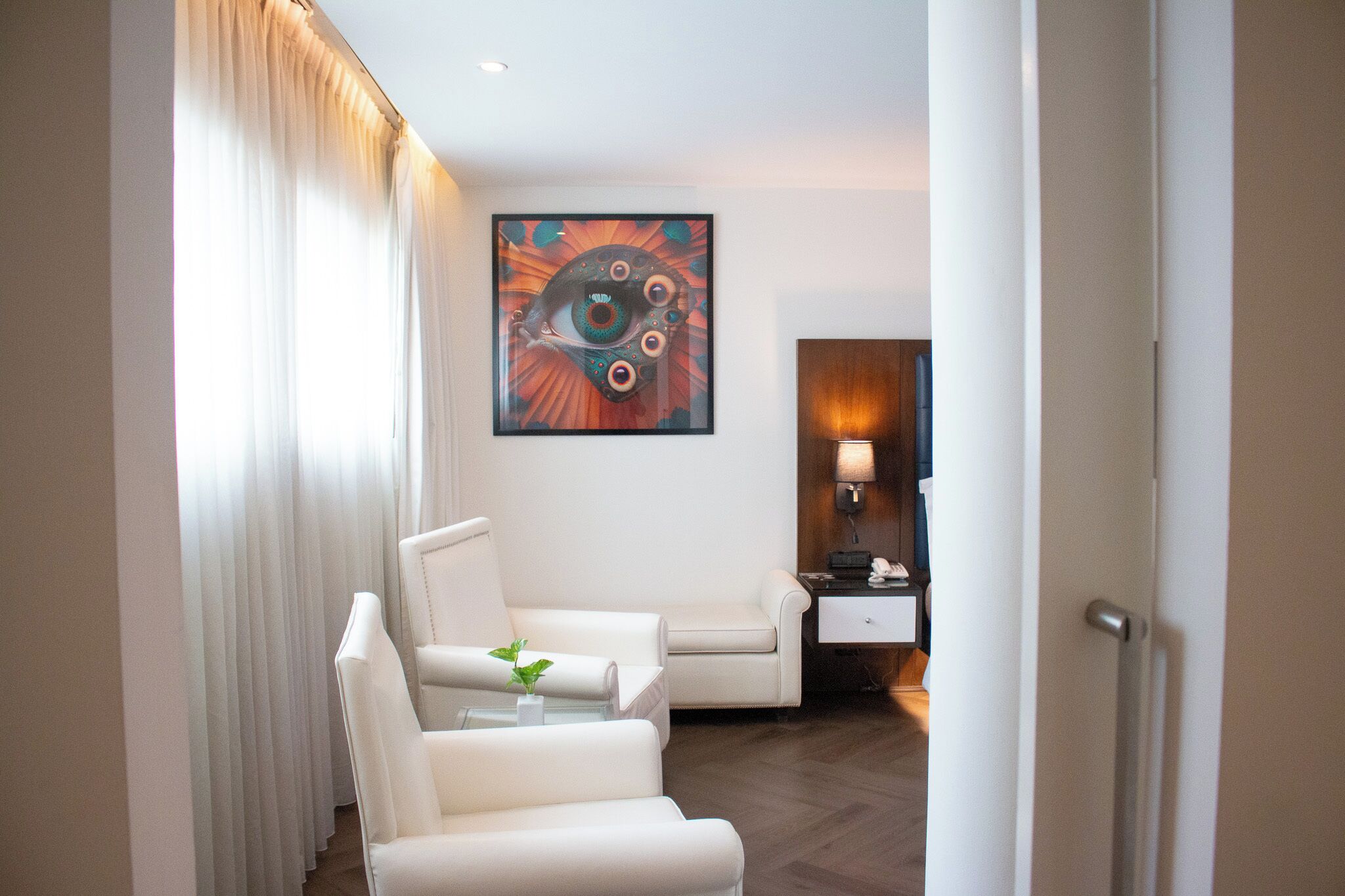 Una habitación de hotel moderna con un sofá de cuero blanco, una mesita con una planta y un cuadro abstracto grande en la pared.
