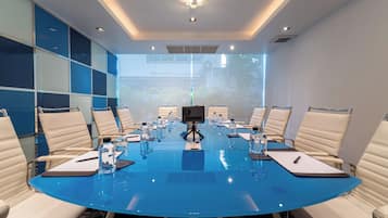 Un salón de conferencias con una mesa azul, sillas blancas y una cámara sobre la mesa.