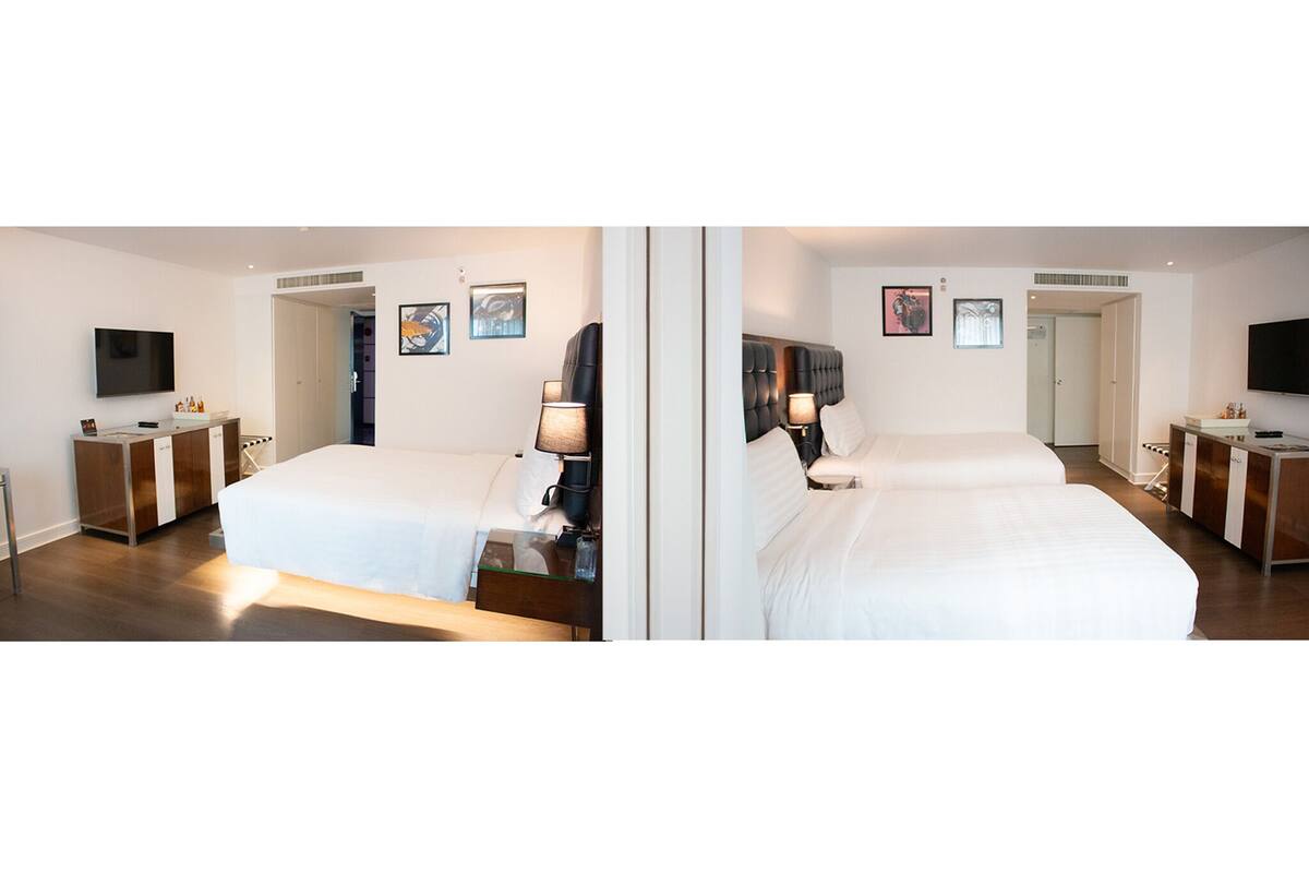 A hotel room with a large bed, bedside tables, a TV, and artwork on the walls.
