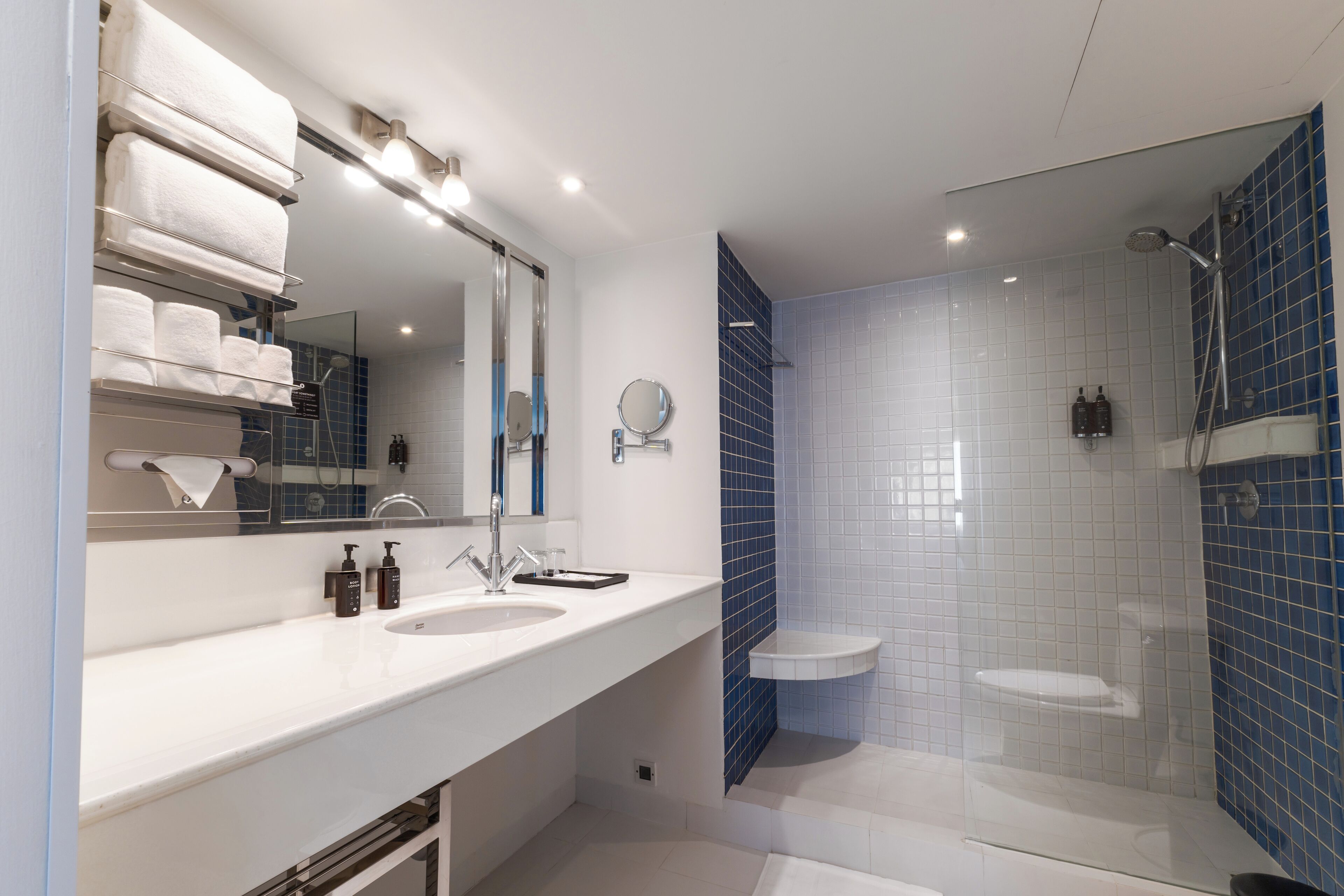 Un baño moderno con dos lavamanos, un espejo grande y una zona de ducha con azulejos azules.
