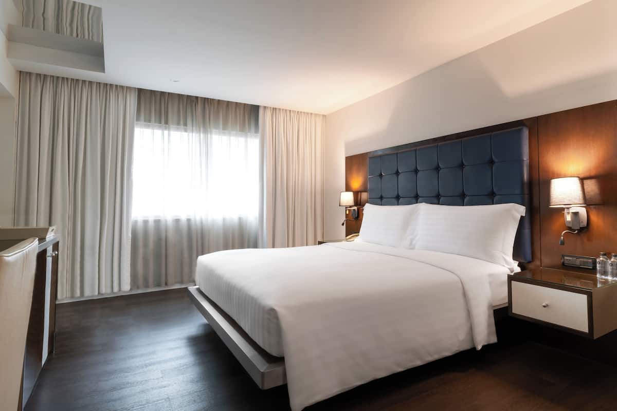 A hotel room with a large bed, two bedside tables with lamps, a built-in headboard, and a large window with curtains.