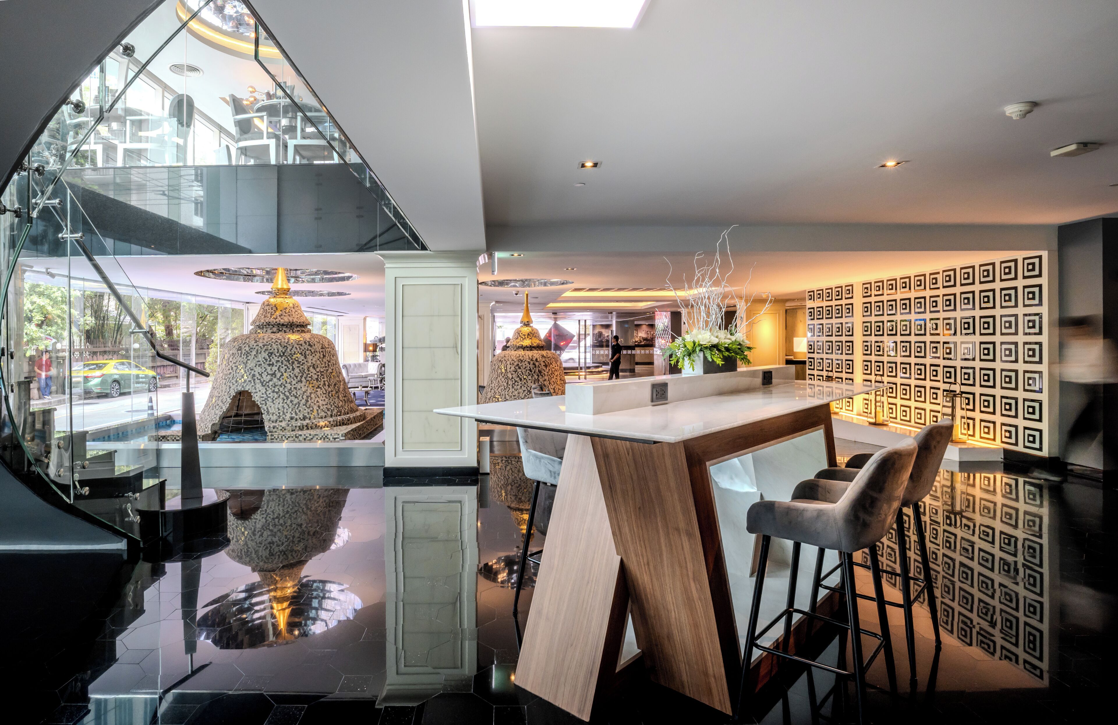 A modern interior with a glass staircase, a wooden bar area, and a patterned wall.
